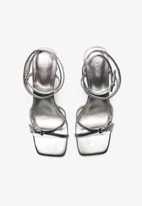 Silver heeled sandals with a metallic finish. Features thin straps and square toe design. Includes a buckle detail for secure fit.