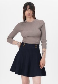 Beige geribbelde langesleeve top gecombineerd met een marineblauwe plissé rok met gouden knopen in de taille. Voorzien van een gladde stofstructuur en een getailleerd ontwerp.