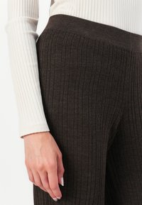 Brown ribbed knit pants with an elastic waistband, paired with a cream ribbed long-sleeve top. Close-up showing texture and fit.
