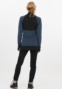 Langærmet atletisk top i blå og sort. Tekstureret stof på den øverste ryg, tætsiddende design, kombineret med sorte bukser og vandresko.