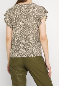 Top de manga corta con un estampado de leopardo en tonos beige y marrones, con mangas con volantes y un corte relajado. Detalle de tejido texturizado.