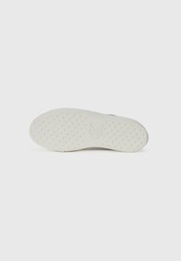White rubber sneaker sole with textured surface, featuring a logo imprint and circular grip patterns. Smooth, minimalist design.