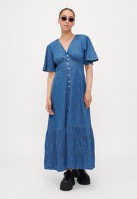 Denim maxi-kjole med korte pufferm, V-hals, frontknapping og lagdelt volangbunn. Mørk blå farge med myk tekstur.