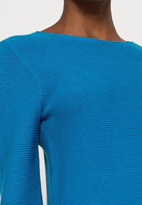 Pull bleu texturé avec un design côtelé, encolure bateau et manches longues, avec une finition lisse et des coutures uniformes.