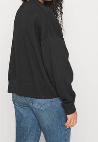 Black sweatshirt with a relaxed fit, ribbed hem, dropped shoulders, and textured fabric, paired with blue jeans.