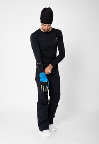 Svart långärmad baslager, marinblå skidbyxor, en svart stickad mössa och blå handskar med svarta accenter, med en säker handledsfäste.