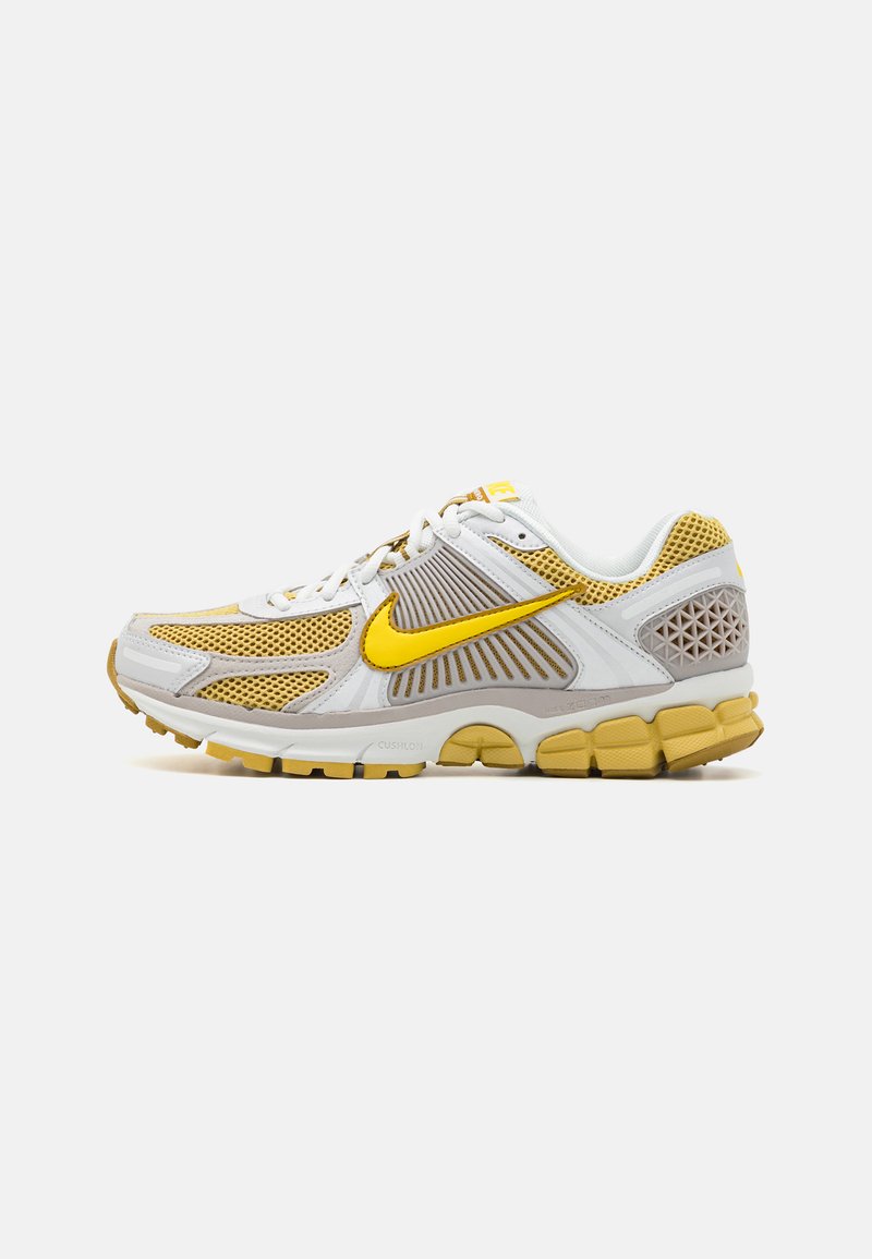 Sapatilha de corrida da Nike com um cabedal em malha branca, detalhes amarelos, sobreposições cinzas, sola acolchoada e painel de calcanhar texturizado.