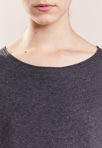 Primo piano della parte inferiore del viso e del collo con pelle chiara, indossando una camicia di tessuto grigio scuro e texture con scollatura ampia.
