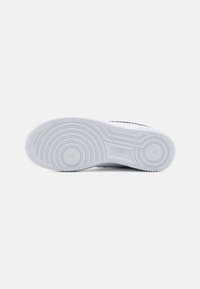 Semelle d'une basket Nike blanche montrant un motif de bande de roulement circulaire et le logo Nike sur un fond plat gris clair.