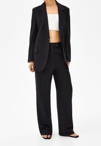 Svart skräddarsydd kavaj med notch-lapel, en lätt axelvadd, kombinerad med högmidjade svarta byxor. Vit ribbad crop top under.