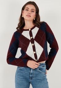 Red, navy, and white argyle-patterned cardigan with long sleeves, round neckline, and gold buttons down the front. Soft, textured knit fabric.