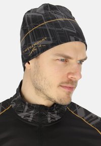 Zwarte beanie met een geometrisch grijs patroon en gouden accenten, gemaakt van rekbaar materiaal, ontworpen voor comfort en warmte.