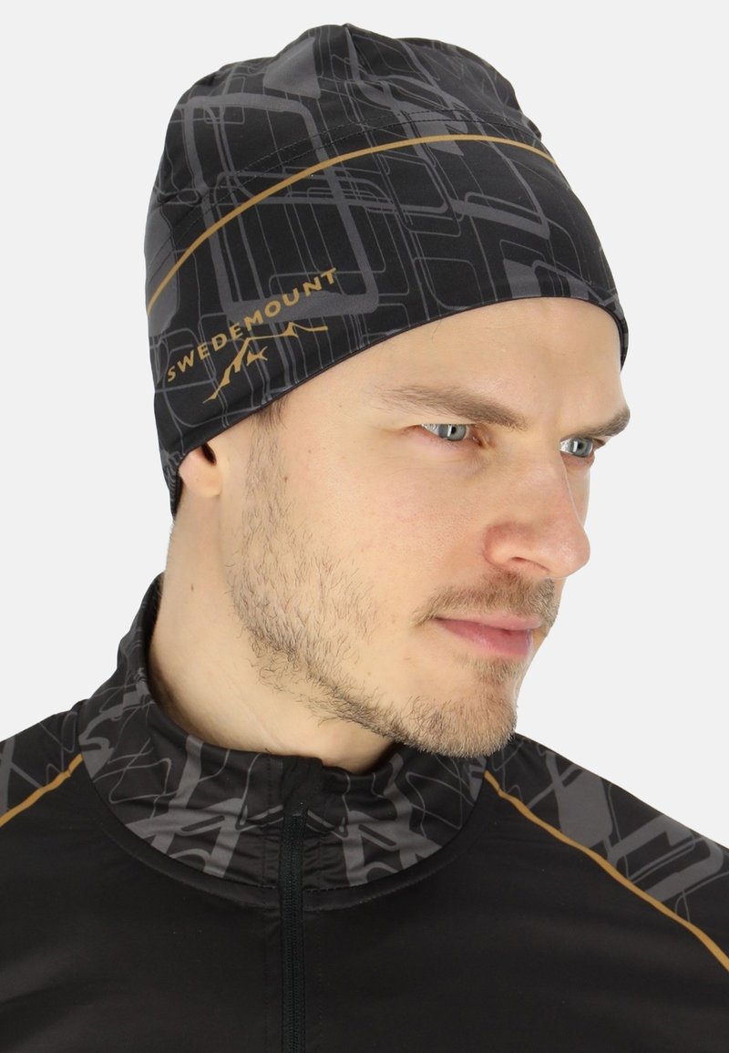 Zwarte beanie met een geometrisch grijs patroon en gouden accenten, gemaakt van rekbaar materiaal, ontworpen voor comfort en warmte.