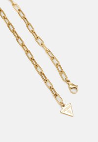 Collier en chaîne dorée avec des maillons allongés, doté d'un fermoir à ressort et d'un pendentif en forme de triangle. Finition lisse et couleur uniforme.
