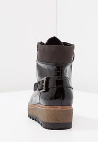 Botte cheville en cuir verni noir avec un col en daim gris, détail de boucle, et une semelle plateformée texturée, présentant un design de semelle en relief.