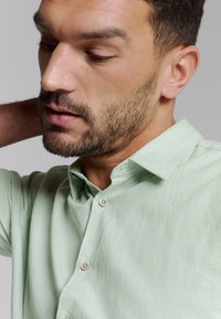 Lichtgroen button-up shirt van een textuurstof. Opvallende details zijn een klein geborduurd logo en een klassieke kraag.