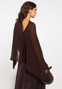 Capa marrón transparente con un profundo escote en V en la parte posterior, mangas fluidas y un diseño en capas. Acompañada por una falda oscura texturizada y un clutch.