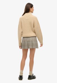 Beige geribbelde trui met hoge kraag, gecombineerd met een geruite mini-jurk in grijs, zwart en geel; enkelsokken en zwarte schoenen.