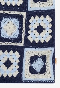 Coperta all'uncinetto a quadretti granny nei toni del blu, bianco e blu navy con motivi geometrici testurizzati su sfondo bianco.