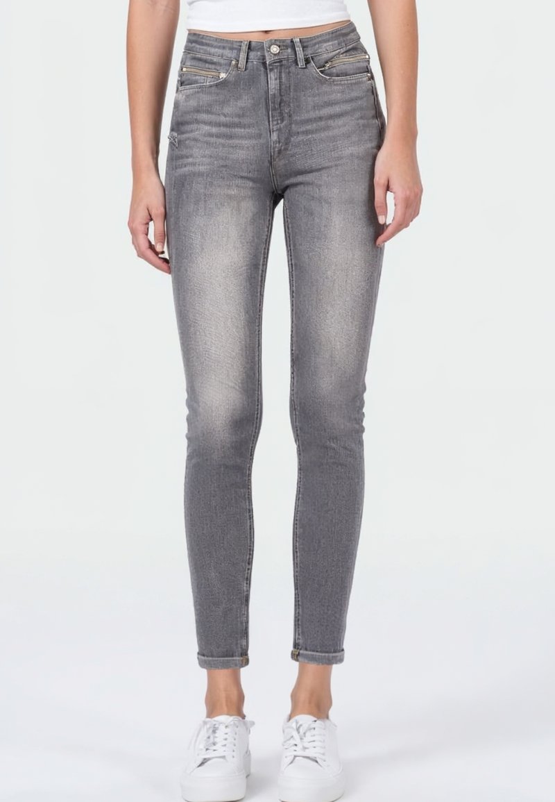 Grijze high-waisted jeans met een slim fit, voorzien van een vervaagde uitstraling, vijf zakken en opgerolde uiteinden, gecombineerd met witte sneakers.