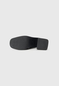 Chaussure à talon haut noire avec un embout carré et un accent en cuir texturé. La semelle en caoutchouc présente un motif de préhension linéaire pour plus de stabilité.