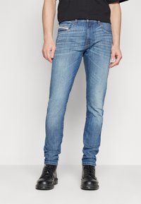 Jean en denim bleu clair avec une coupe slim, comprenant des poches standard, un petit logo à l'arrière, associés à des bottes noires à lacets.