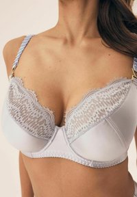Light blue bra with lace detailing and scalloped edges, featuring textured straps and gold hardware accents. Smooth satin finish.