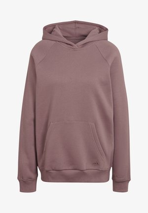 Osoba nosící fialovo-růžovou mikinu Adidas a odpovídající tepláky, s rukou v kapse mikiny, oříznuto na úrovni krku a stehen.