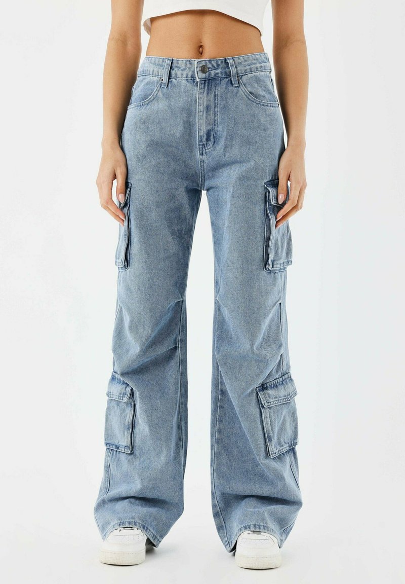 Pantalons cargo en denim bleu clair avec jambes larges, présentant plusieurs poches latérales et une fermeture à bouton classique. Texture douce et coupe décontractée.
