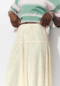 Jupe en dentelle crème avec motif floral, taille élastique et design à superpositions. Portée avec un haut à rayures vertes et roses.