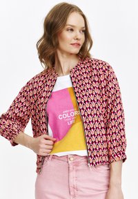 Rot- und rosa gemusterte Jacke mit Reißverschluss vorne, Rundhalsausschnitt und gerafften Ärmeln, getragen über einem mehrfarbigen Grafik-T-Shirt.