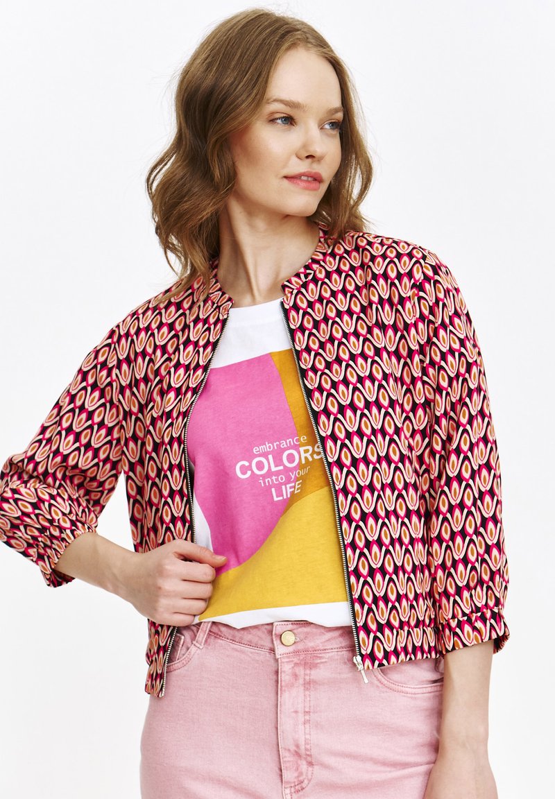 Rot- und rosa gemusterte Jacke mit Reißverschluss vorne, Rundhalsausschnitt und gerafften Ärmeln, getragen über einem mehrfarbigen Grafik-T-Shirt.