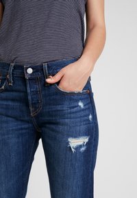 Donkerblauwe spijkerbroek met een rechte snit, lichte slijtage op de dij en een klassieke vijf-pocketontwerp met contrasterende stiksels.