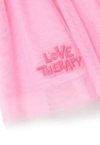 Roze tule stof met een geborduurd "Love Therapy" logo in een speelse lettertype, gekenmerkt door een zachte, doorzichtige textuur en gelaagd ontwerp.