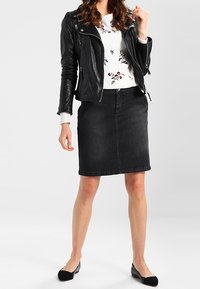 Chaqueta de moto de cuero negra sobre un suéter blanco con bordado floral, combinada con una falda de mezclilla negra y bailarinas negras.