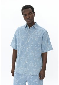 Camicia in denim azzurro chiaro a maniche corte con motivo floreale, chiusura frontale a bottoni, tasca sul petto e vestibilità comoda.