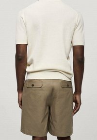 Beżowy sweter z prążkowanego materiału z krótkim rękawem w zestawie z khaki szortami, które mają dwie tylne kieszenie zapinane na guziki.