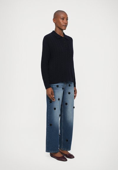 Marineblå strikket polo genser med en treknapps placket, kombinert med lyseblå vide jeans med blomsterapplikasjoner. Burgunder leppestift.