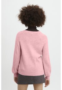 Rosa stickad tröja med mjuk textur, raglanärmar och ribbade muddar. Bakstycket har en rundad halsringning och en något längre fåll.