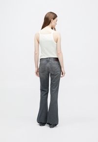 Γκρι τζιν παντελ�όνι καμπάνα με μέση μέτριου ύψους, πίσω τσέπες και ελαφριά υφή. Συνδυασμένο με απλή λευκή φανέλα.