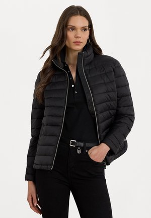 Giubbotto a vento nero con colletto alto, design a righe orizzontali, chiusura con zip e logo ricamato. Indossato sopra una polo nera e jeans.