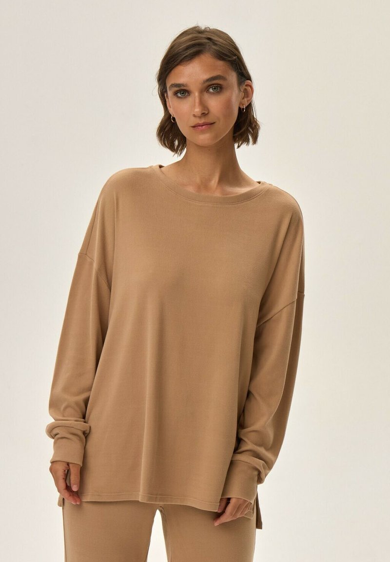 Beżowa bluzka z długim rękawem o luźnym kroju, okrągłym dekolcie i podwiniętych mankietach. Miękka tkanina i boczne rozcięcia zwiększają komfort i swobodę ruchów.