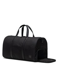 Mustassa kangasta valmistettu duffel-laukku, jossa on nahkakahvat, pyöreä muoto, vetoketjukiinnitys ja sivuaukko helppoa pääsyä varten.