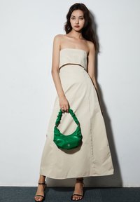 Beiges trägerloses Kleid mit hoher Taille und knöchellangem Design. Eine grüne geraffte Handtasche und schwarze Riemchensandalen vervollständigen den Look.