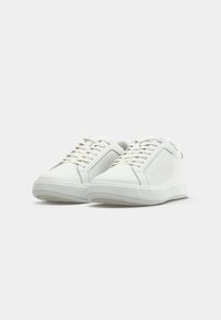 White sneakers made of smooth leather with logo pattern on the side, flat laces, and a thick rubber sole for added comfort.