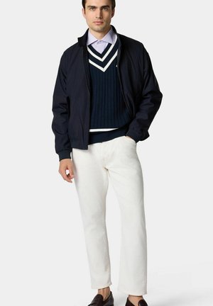 Marine bommenjack over een marineblauw en wit gestreept sweater, gecombineerd met witte broek en bruine loafers. Katoenen materialen met een gladde textuur.