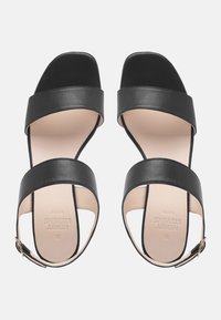 Zwarte leren sandalen met brede banden, vierkant te ontwerp en open hiel. Voorzien van een gouden gesp en een gladde beige binnenzool met logo.