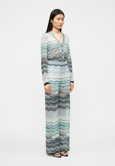 Dolga kombinezona z večbarvnim cik-cak vzorcem v modri, črni in beli barvi, z V-izrezom in gumbi spredaj. Teksturno, lahkotno blago.