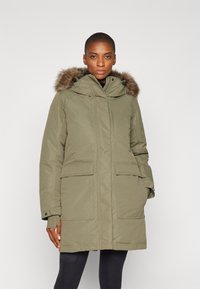 Olijfgroene parka met een bontvoering in de capuchon, een rits aan de voorkant, twee grote zijzakken en elastische manchetten. Glad materiaal met een waterafstotende afwerking.