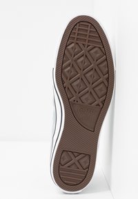 Semelle de sneaker en caoutchouc marron avec un motif en diamant, présentant un bord blanc et un label "Converse All Star" dans un design circulaire.